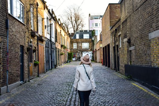 Woman strolling through a charming cobblestone alley in London, England.