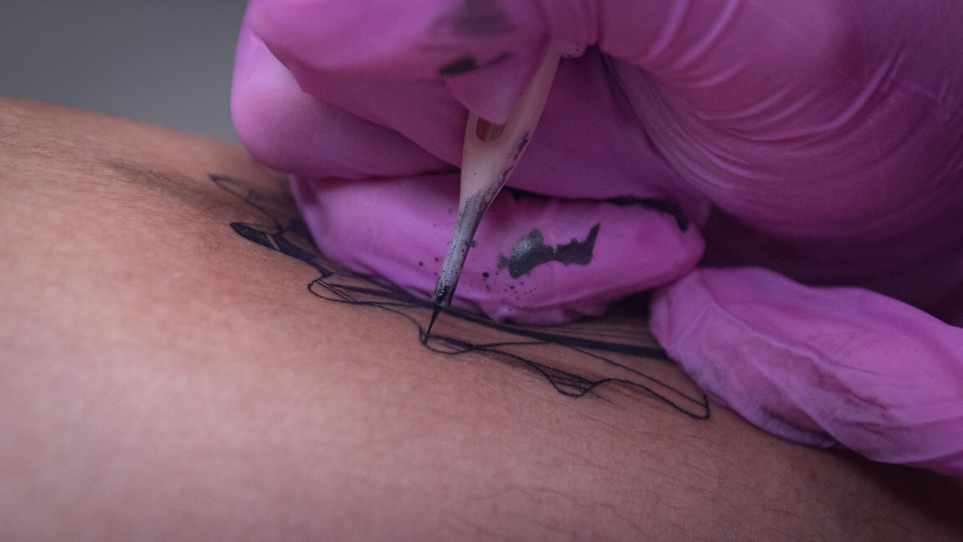 Close-up view of a tattoo artist inking a design on human skin.
