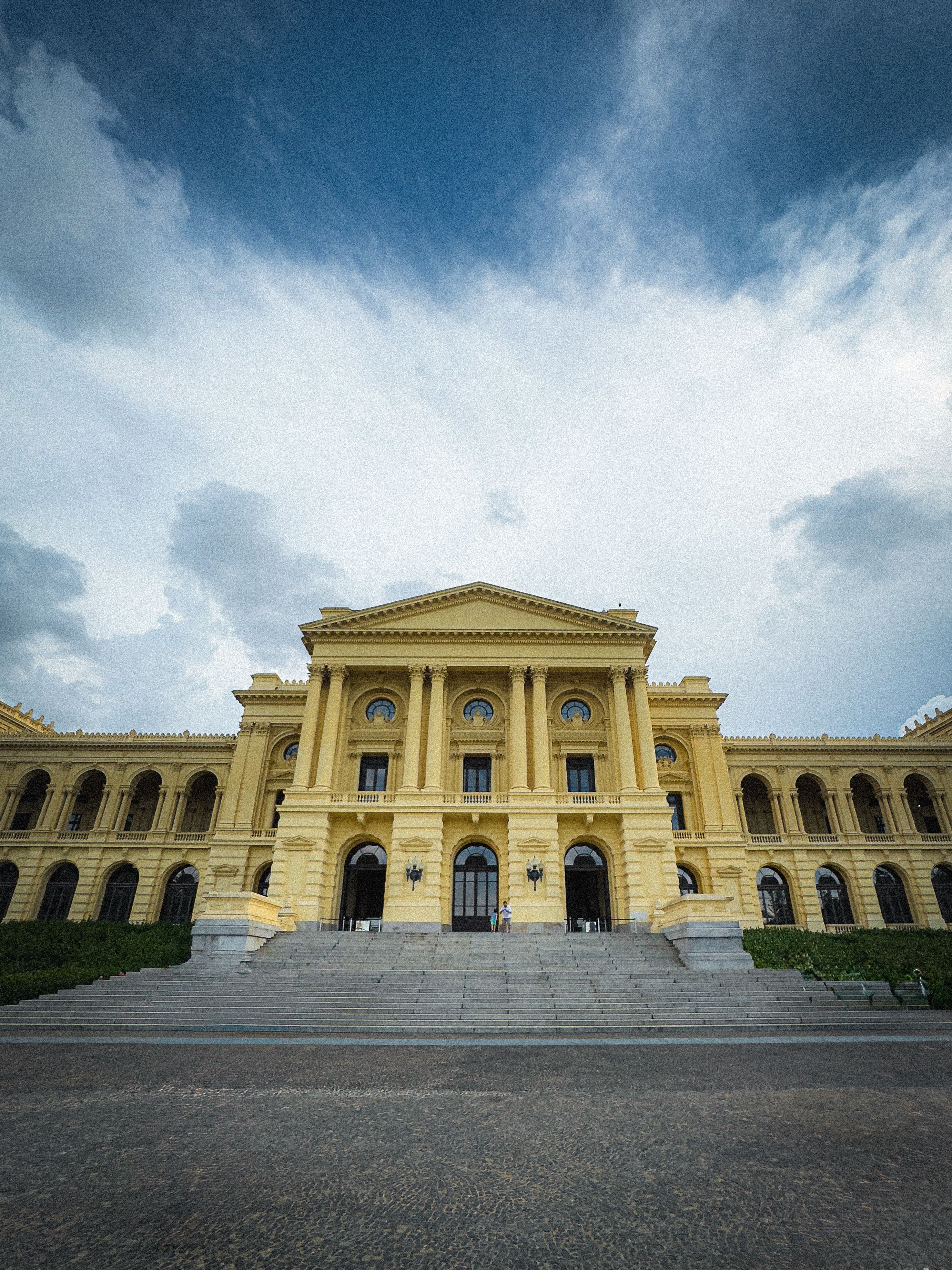 Bezpłatne Majestatyczny żółty, zabytkowy budynek na tle zachmurzonego nieba, podkreślającego piękno jego architektury. Zdjęcie z galerii