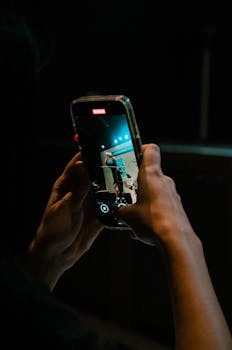 A person films a live sports event on a smartphone in a dimly lit arena.