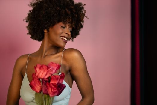 Charming portrait of a smiling woman holding red flowers, set against a soft pink background.
