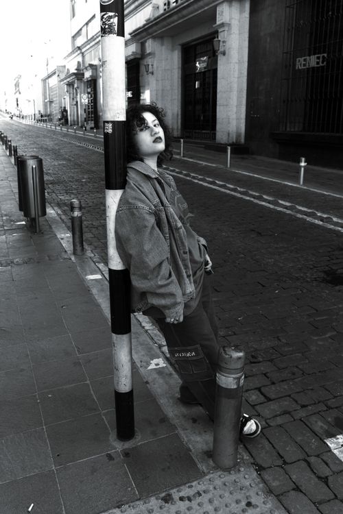 Free A person leans casually against a pole on a quiet city street, embracing urban fashion. Stock Photo