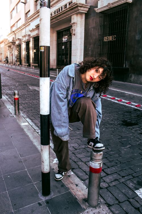 Free Teenager in urban street style poses on cobblestone street with vintage buildings. Stock Photo