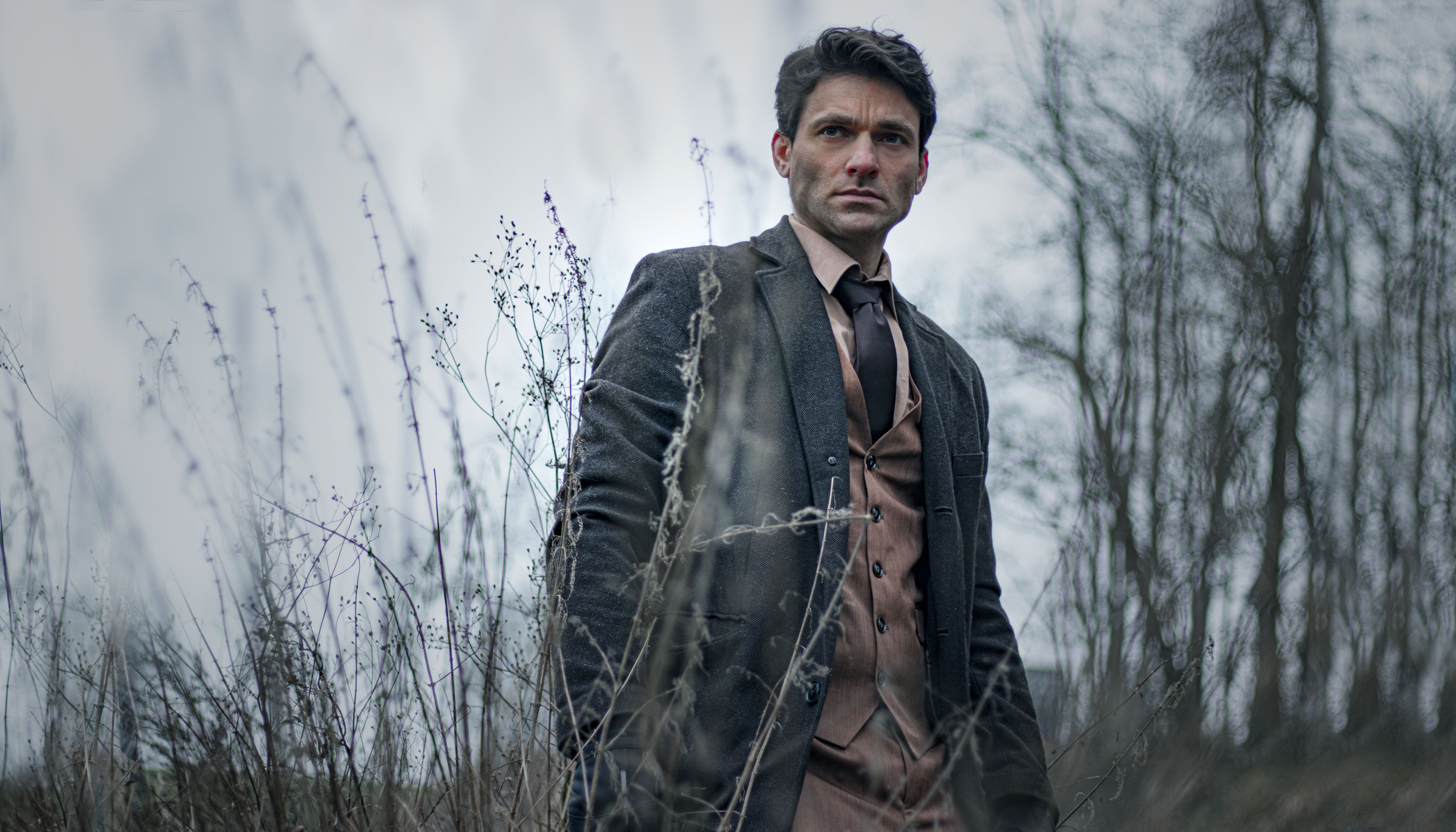 A man in a suit stands in a winter landscape, conveying a moody atmosphere.