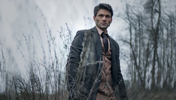 A man in a suit stands in a winter landscape, conveying a moody atmosphere.