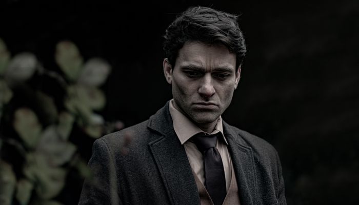 A pensive man in a dark suit standing outdoors. Photo by Vincent Santamaria on Pexels