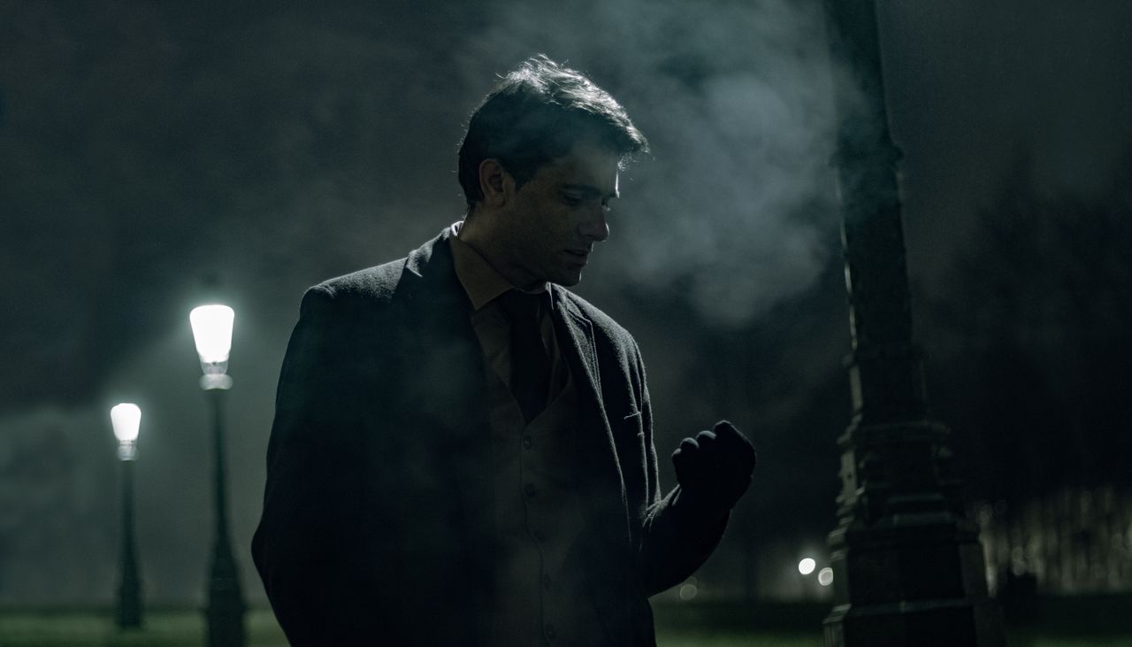 silhouetted man in formal wear standing by lamp posts on a foggy night