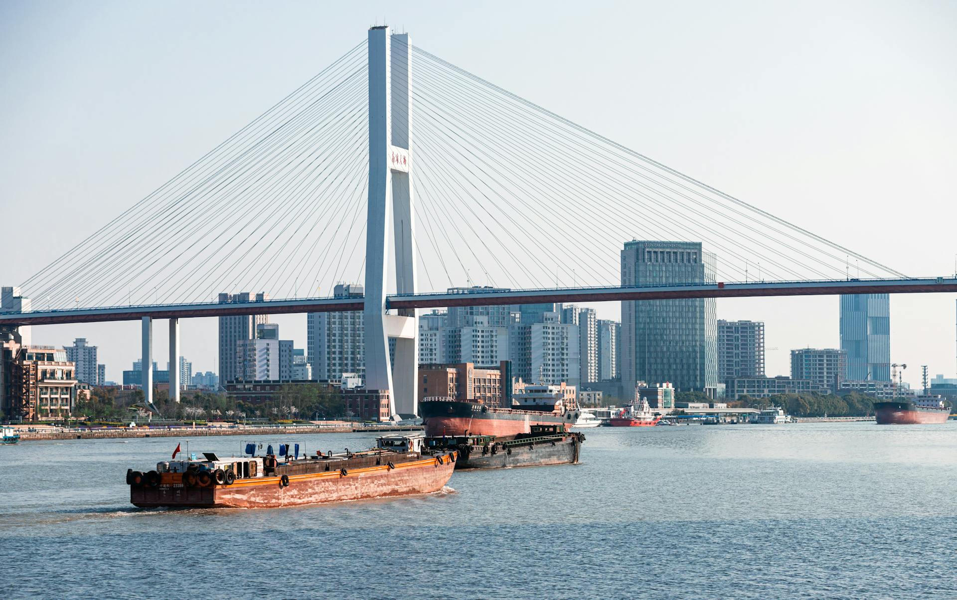 Cargo ship navigating the river under Lupu Bridge with Shanghai skyline in the background.