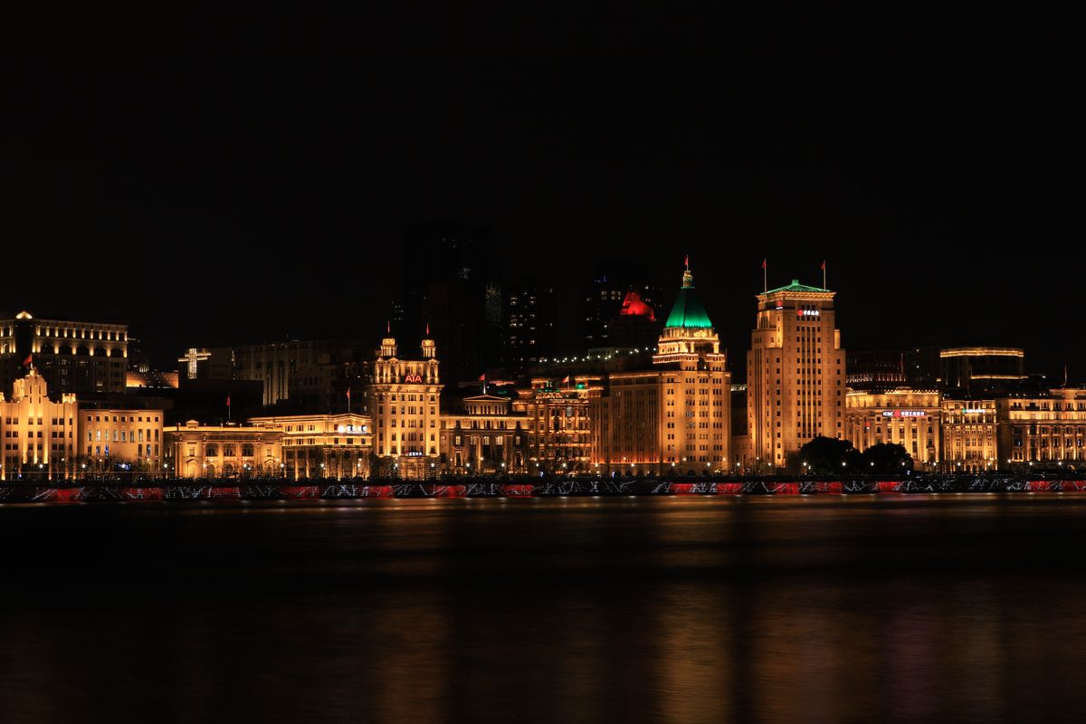 Illuminated colonial buildings along Shanghai's Bund waterfront at night beside the Huangpu River