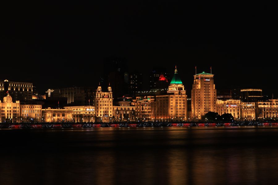 Nighttime skyline of Shanghai's Bund with illuminated historic buildings reflected in the river