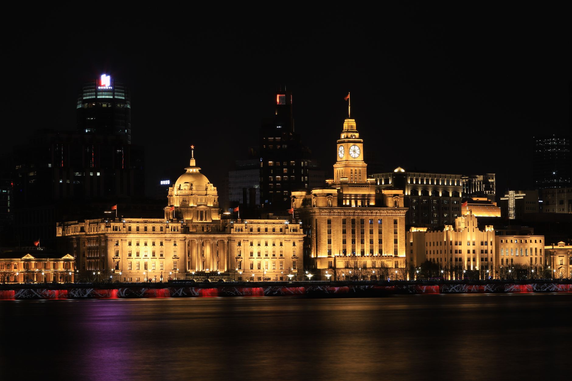 Illuminated historic buildings along The Bund in Shanghai at night, reflecting over water.