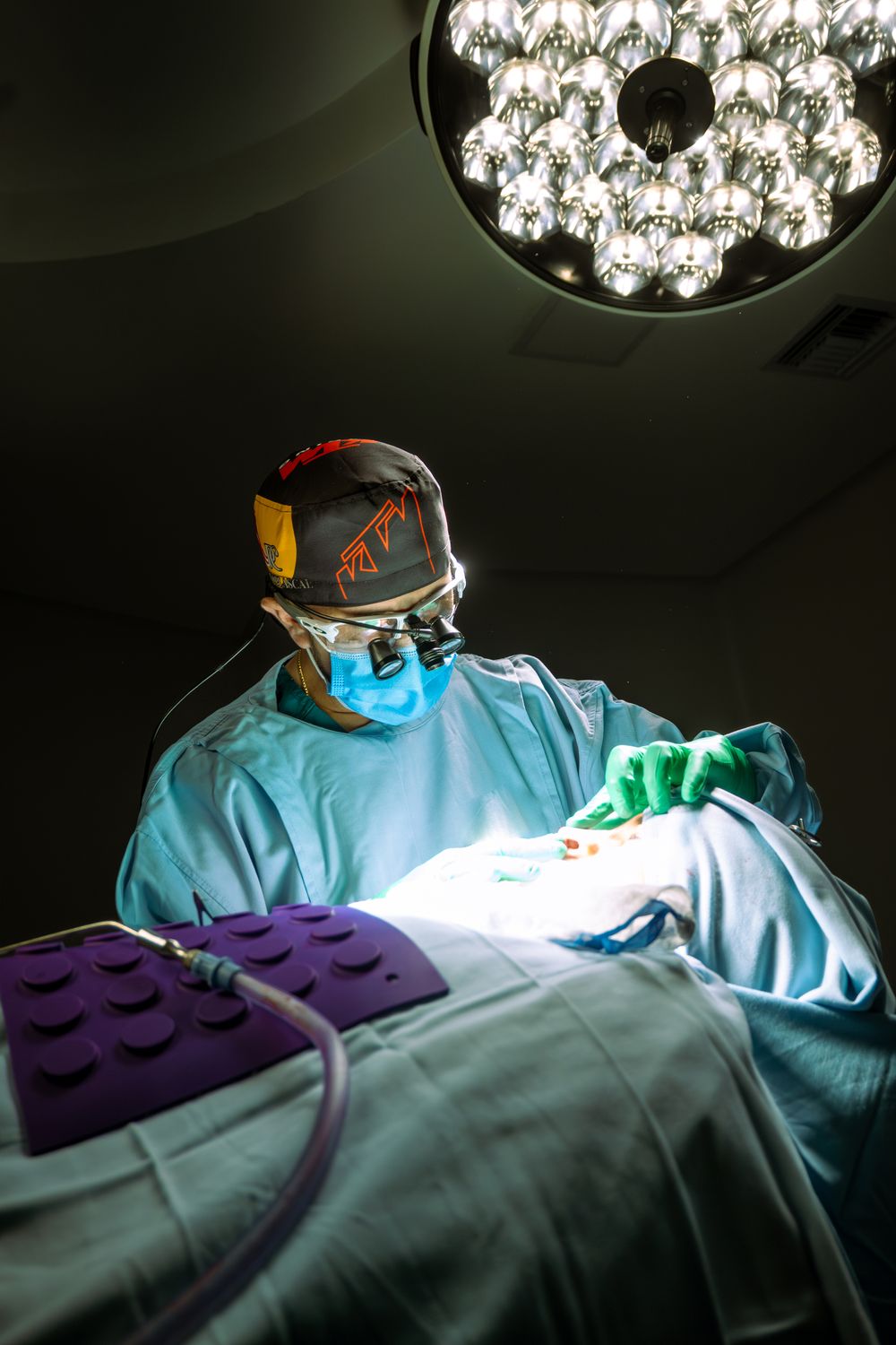 Surgeon performing rhinoplasty beneath operating lights in a sterile theatre