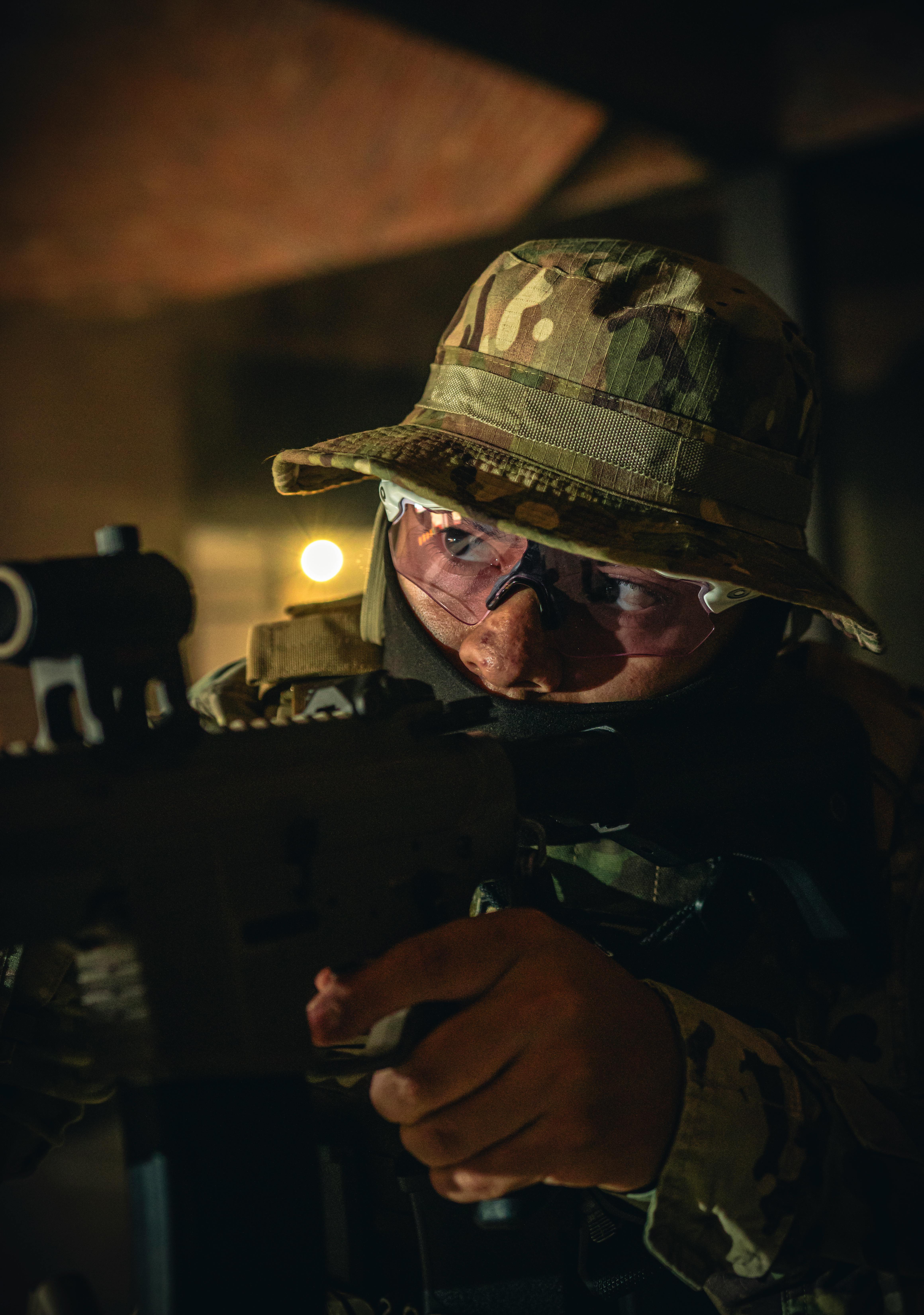 Close-up of a soldier in camo with a rifle indoors.