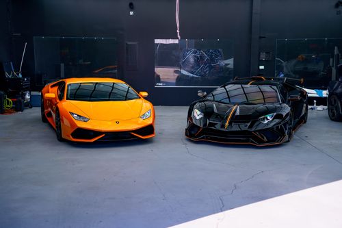 Free Two luxury sports cars, orange and black, parked in a stylish indoor garage. Stock Photo