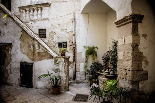 Explore a beautiful rustic courtyard in Apulia, Italy, featuring stone architecture and lush potted plants.