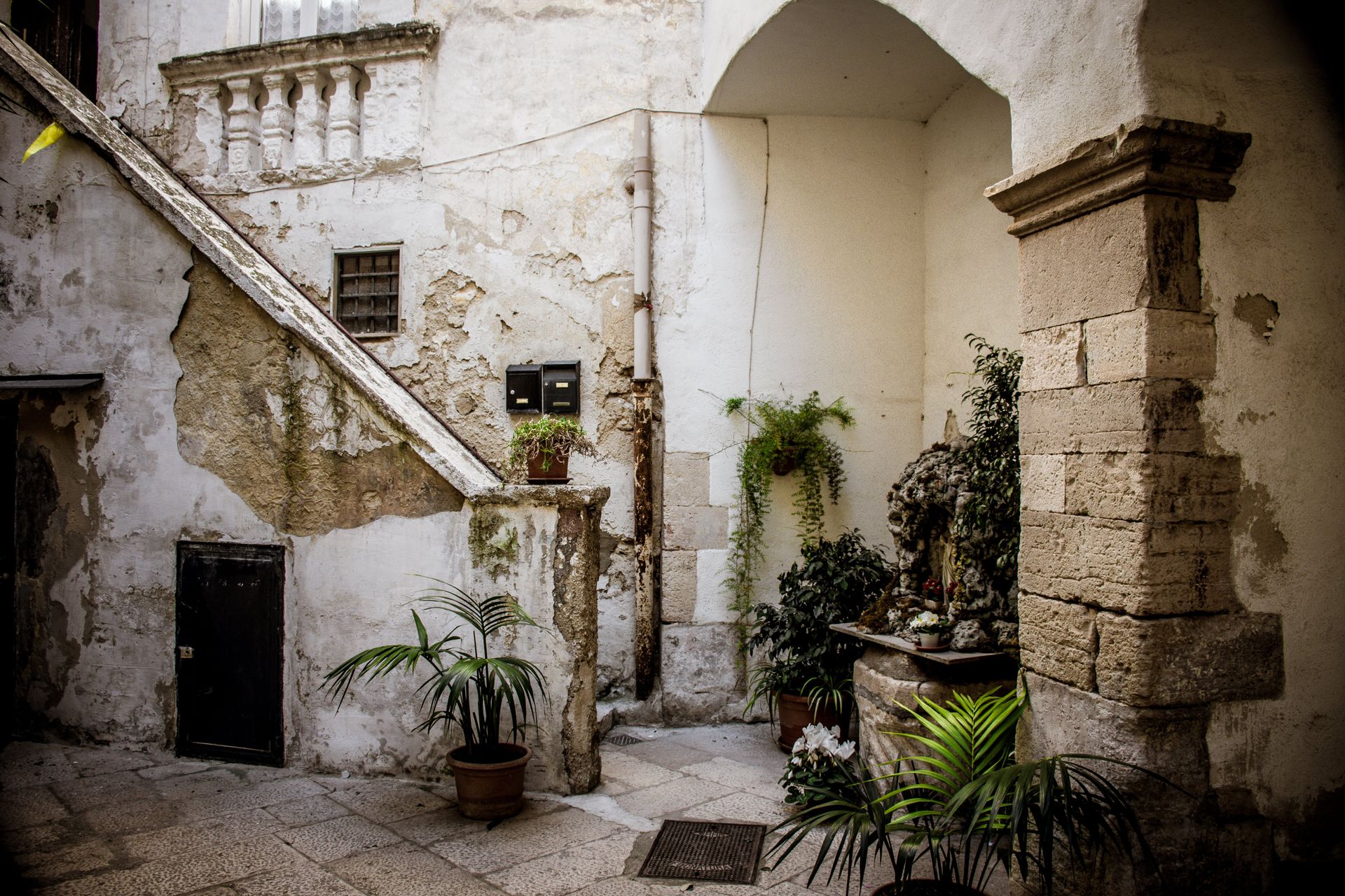 Explore a beautiful rustic courtyard in Apulia, Italy, featuring stone architecture and lush potted plants.