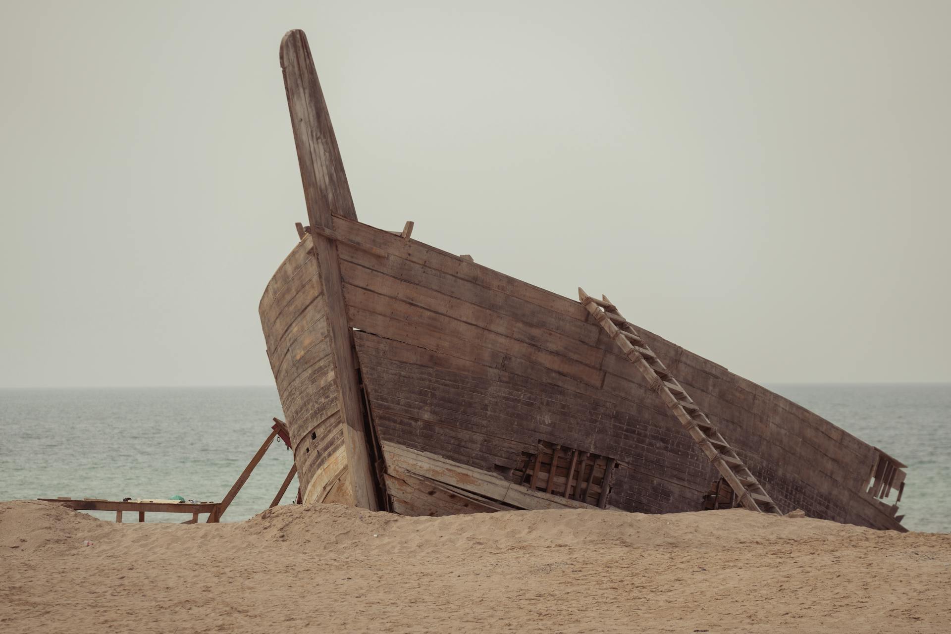 Rustic wooden shipwreck resting on a sandy beach with the ocean in the background.