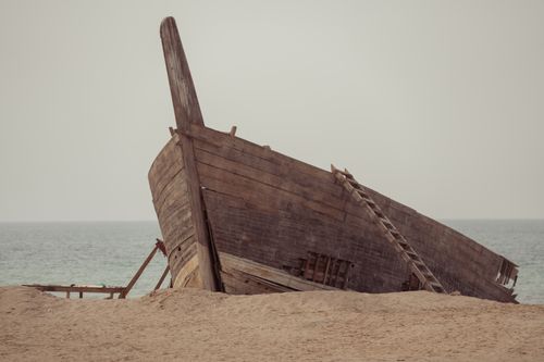Free Rustic wooden shipwreck resting on a sandy beach with the ocean in the background. Stock Photo