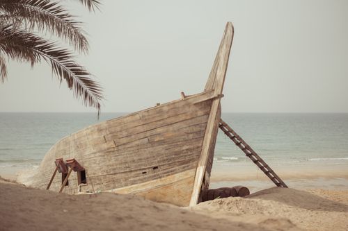Free Weathered wooden boat on a serene deserted beach lined with palm trees. Stock Photo