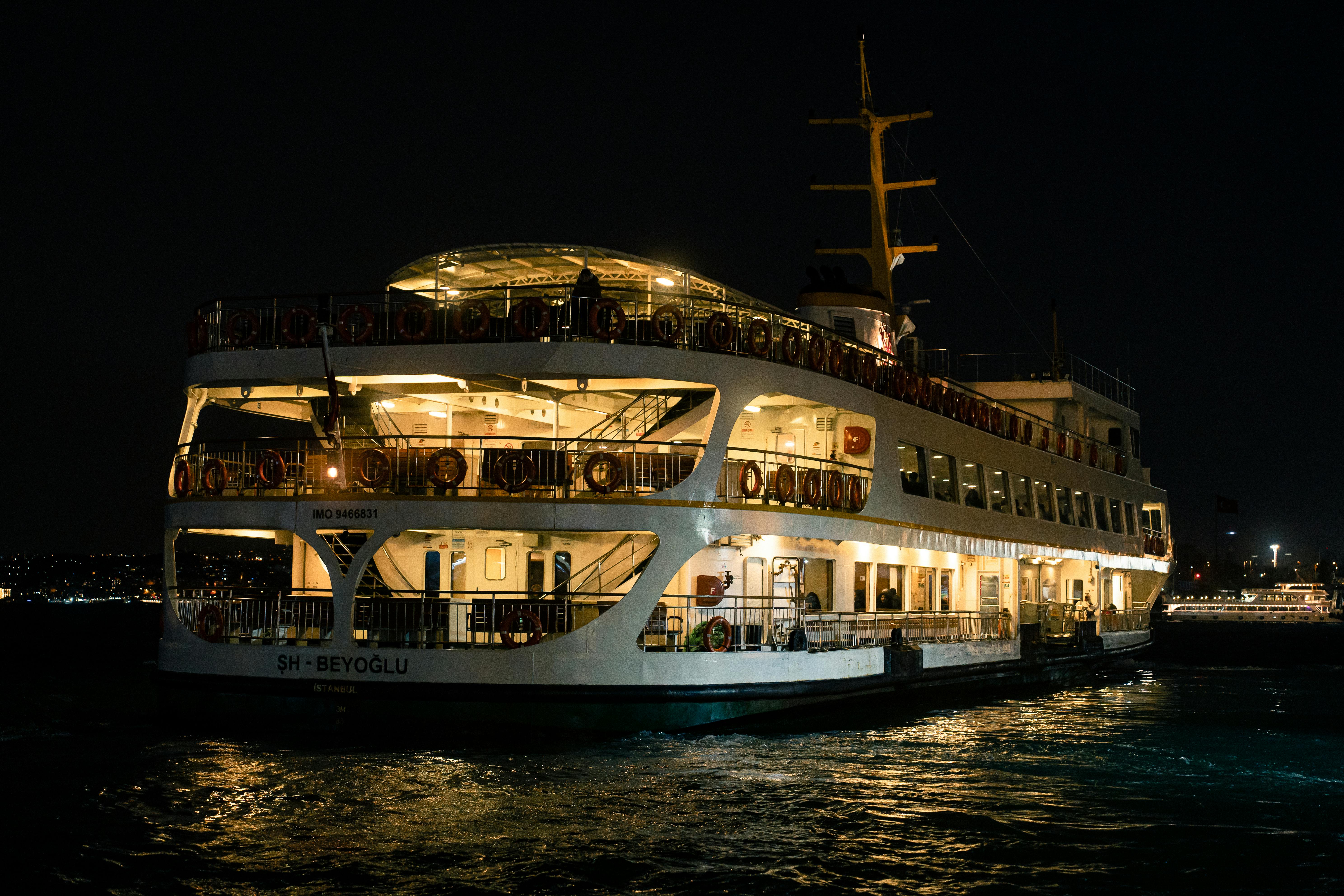 A brightly lit ferry sails through a cityscape at night, creating a vibrant scene.