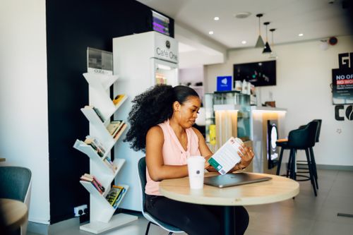 Free Black woman reading a book in a modern Lagos cafe, relaxed and focused atmosphere. Stock Photo