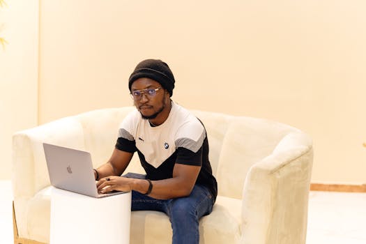 A man sitting on a couch using a laptop, showcasing casual work productivity indoors.