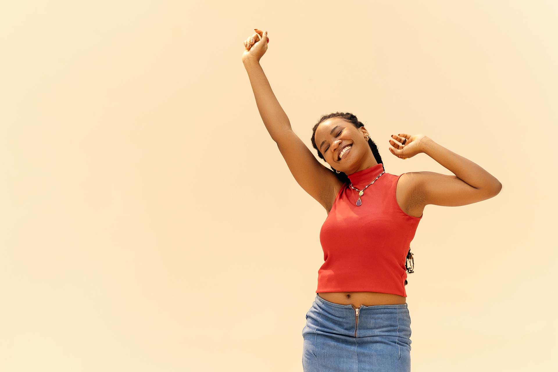 A young woman with a positive spirit in a red tank top and denim skirt smiles and stretches her arms. Find more afrocentric images on www.ninthgrid.com