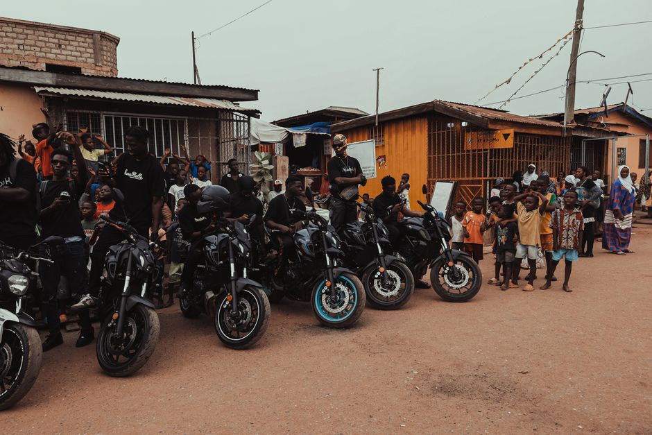 Outdoor gathering of motorcycle enthusiasts and locals on a street in Accra, Ghana.