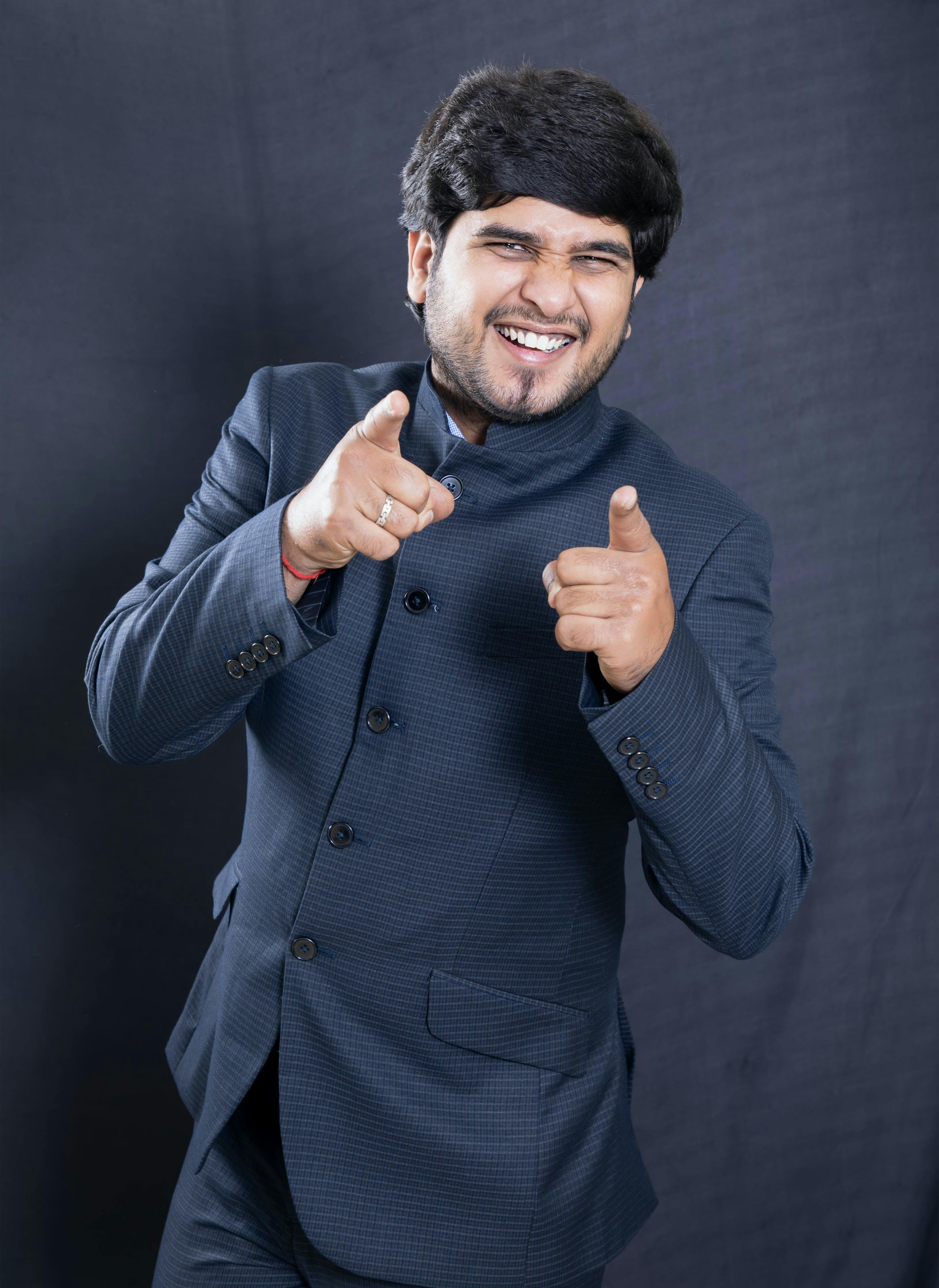 Cheerful young man in a blue suit pointing energetically with a joyful expression.