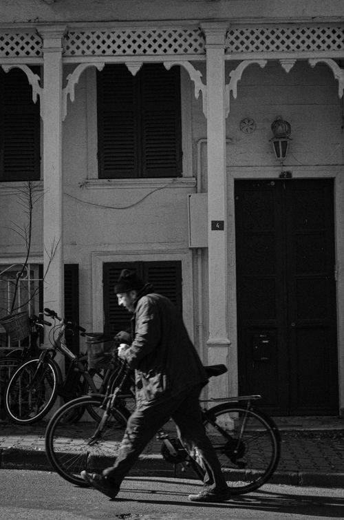 Free A man walks his bicycle past a vintage building with ornate details. Stock Photo