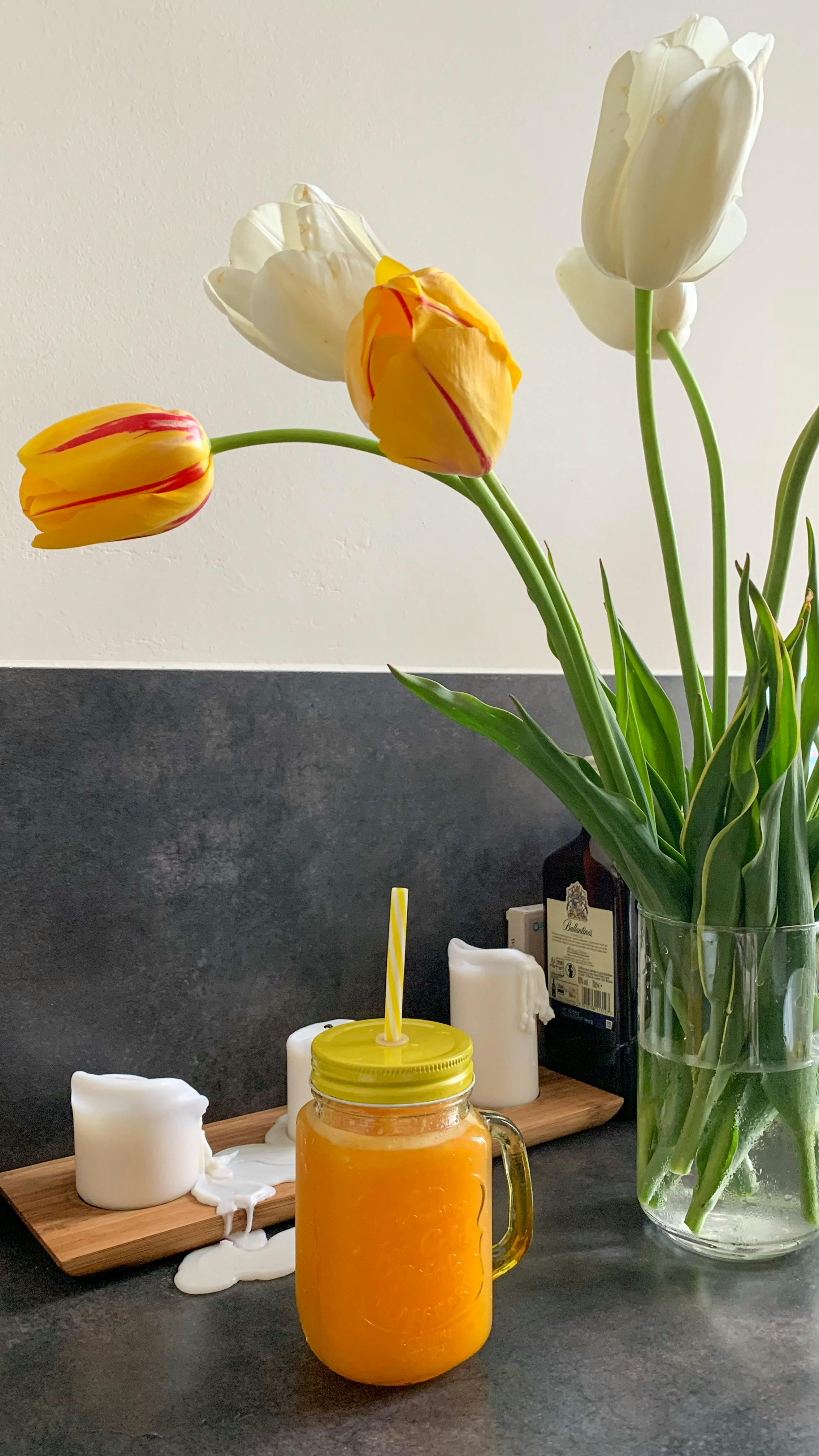 Colorful tulips in vase with fresh orange juice in mason jar on table.