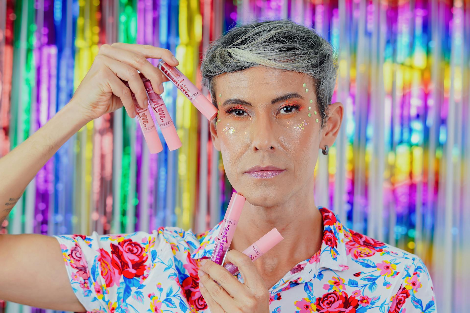 Close-up portrait with colorful makeup and glitter on a vibrant backdrop.