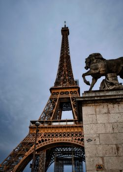 Iconic view of the Eiffel Tower with a statue on a cloudy day in Paris.