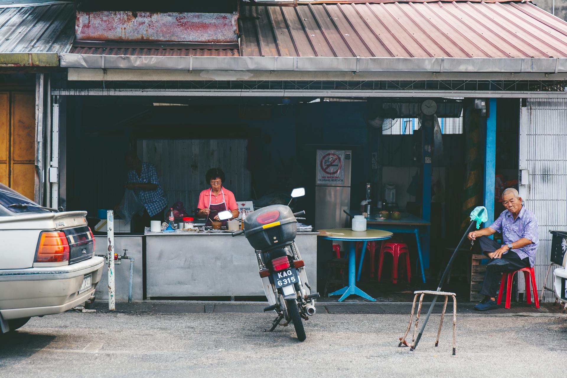 Street view of an outdoor market with people and motorcycle in an urban setting.