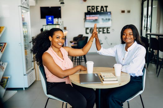 Two women high-fiving to celebrate success in a modern Lagos café, surrounded by books and coffee.