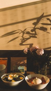 Warm breakfast scene with flowers, books, and morning shadows on the wall.