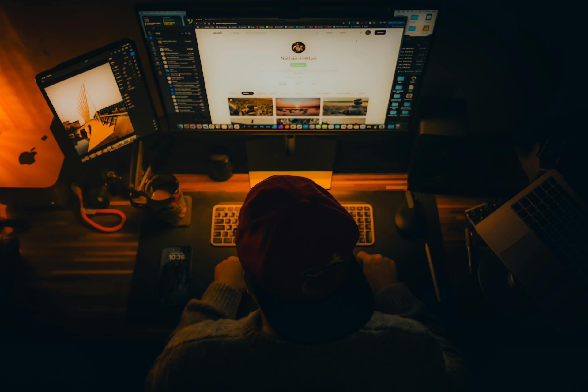 Warm lit home office setup with computers and gadgets, ideal for creative work.