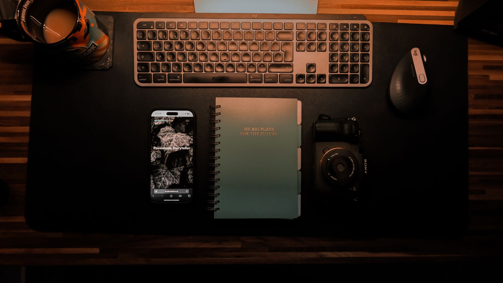 Top-down organized desk with a keyboard, camera, notebook and smartphone
