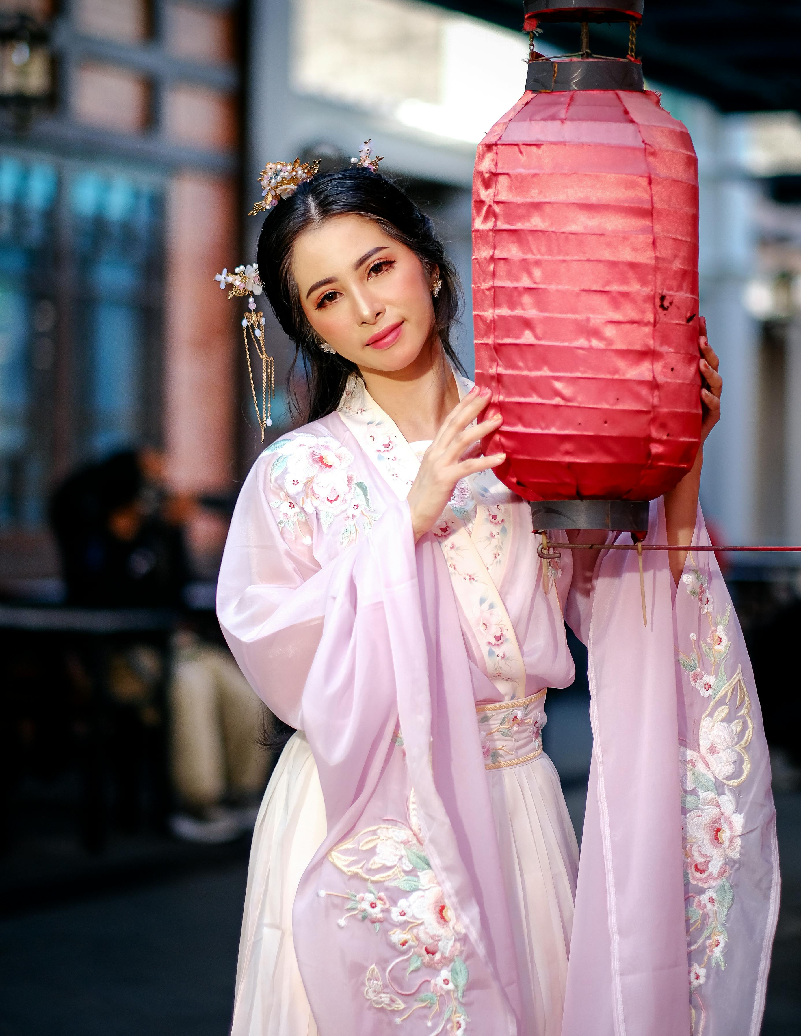 Woman in a traditional Hanfu dress holding a red lantern, symbolizing Chinese culture and festive celebration.