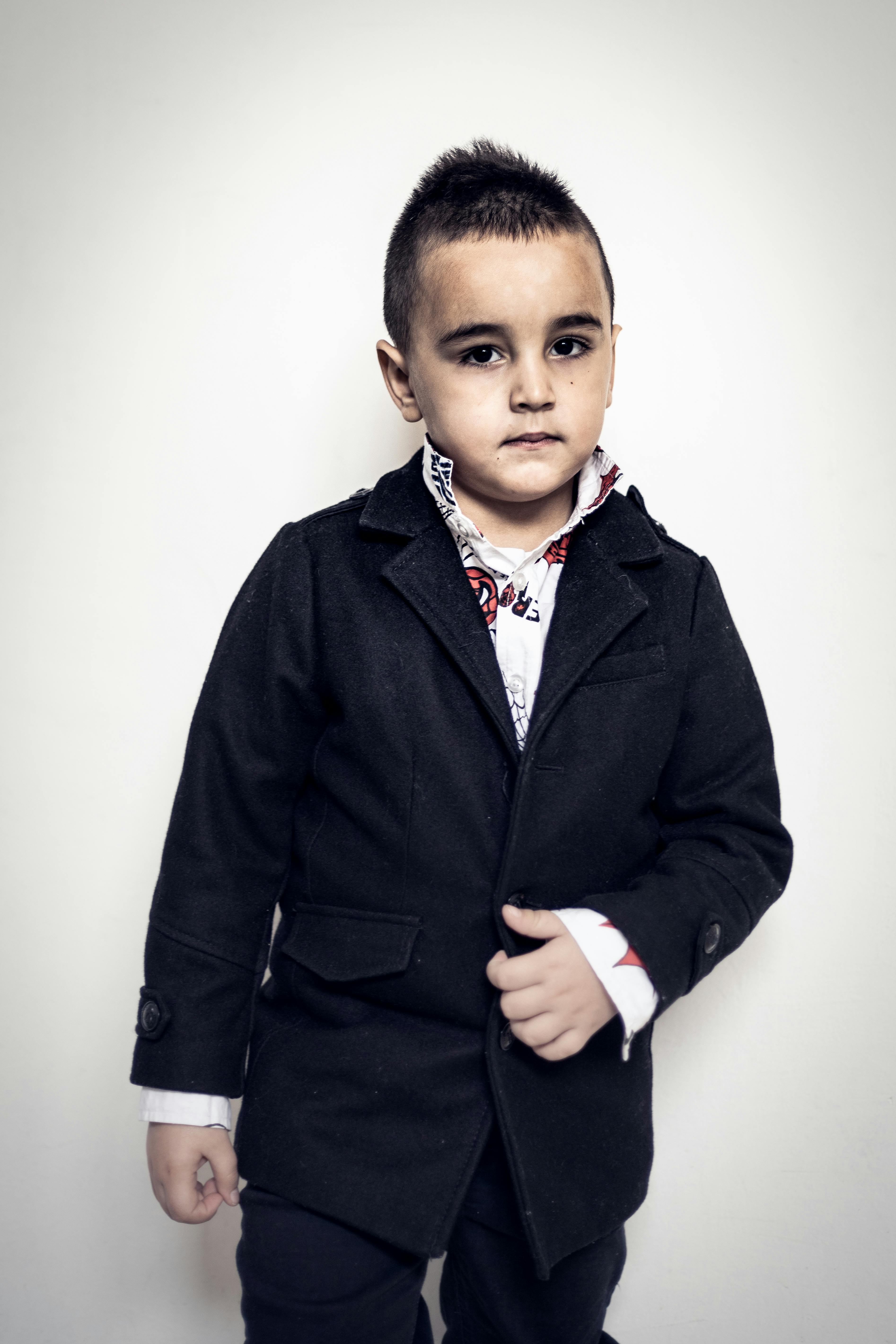 bezplatná Sebevědomý mladý chlapec ve formálním černém obleku pózuje na světlém pozadí. Základová fotografie