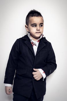 Young boy in a stylish black jacket and printed shirt posing confidently.