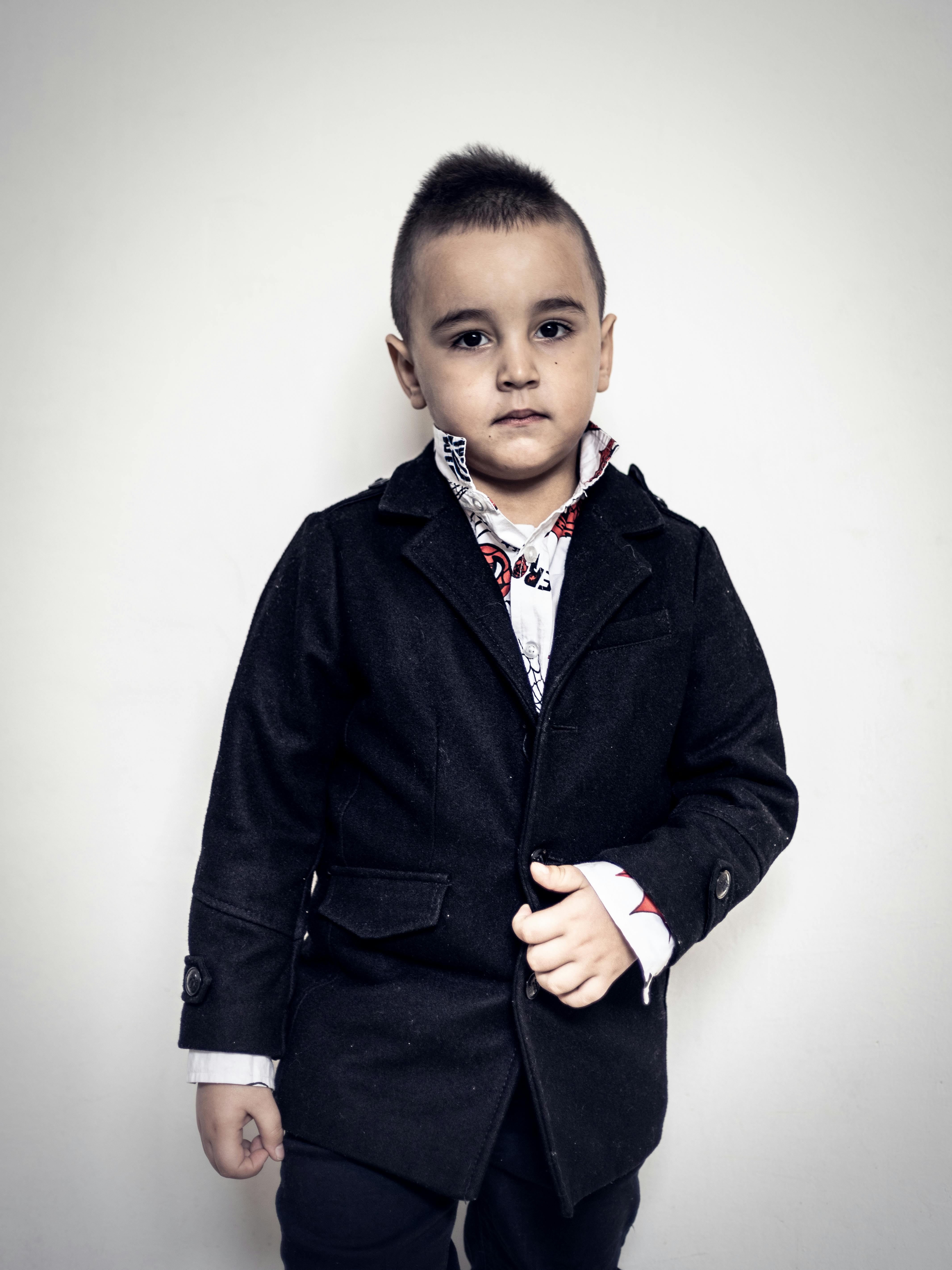 Free Portrait of a young boy wearing a chic black coat with a serious expression. Stock Photo