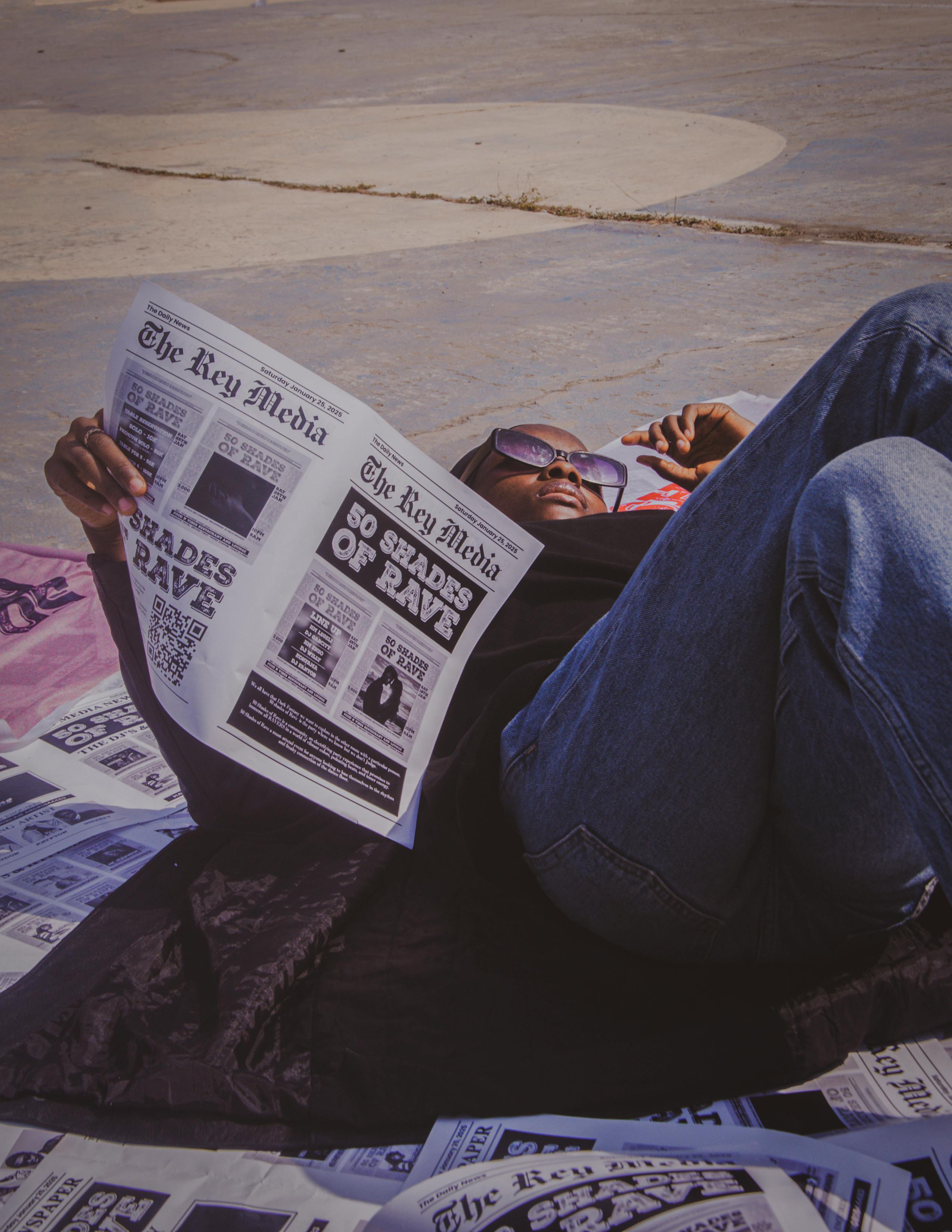 man relaxing on a blanket reading a newspaper outdoors