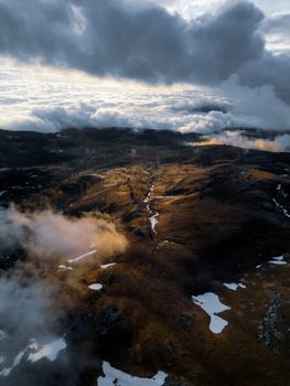 Stunning aerial view of a mountainous landscape with dramatic clouds and snow patches at sunset.