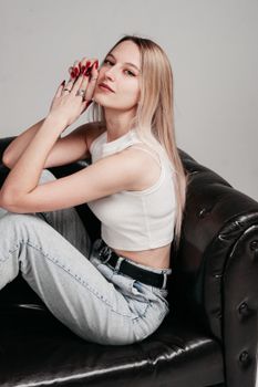 Fashionable young woman sitting on a leather couch, exuding relaxed confidence.