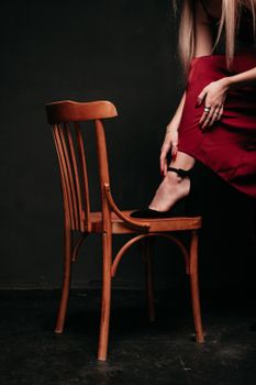 A chic woman in a red skirt adjusts her outfit gracefully on a classic wooden chair.