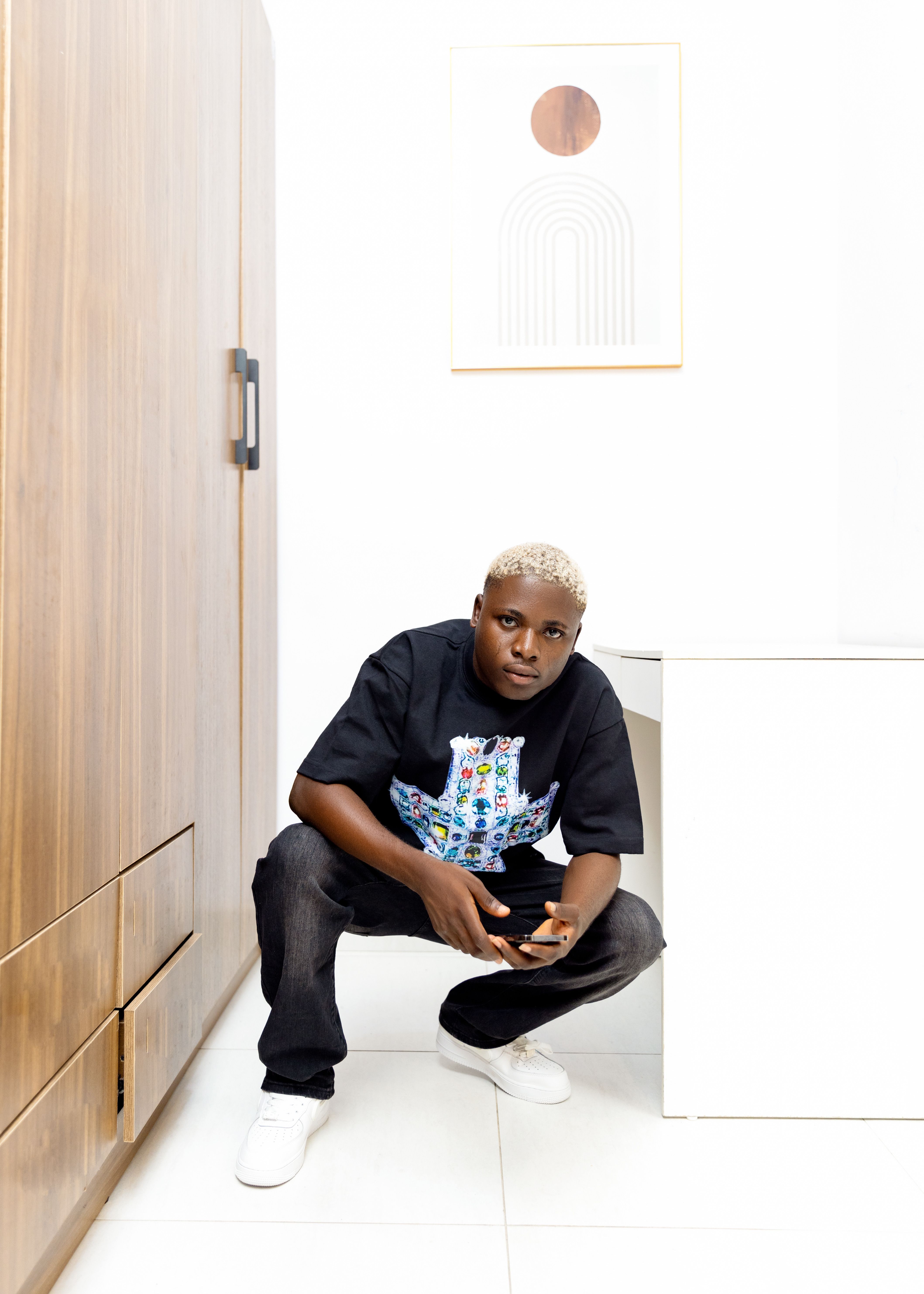 Young man crouching in a modern, minimalist room with stylish decor.