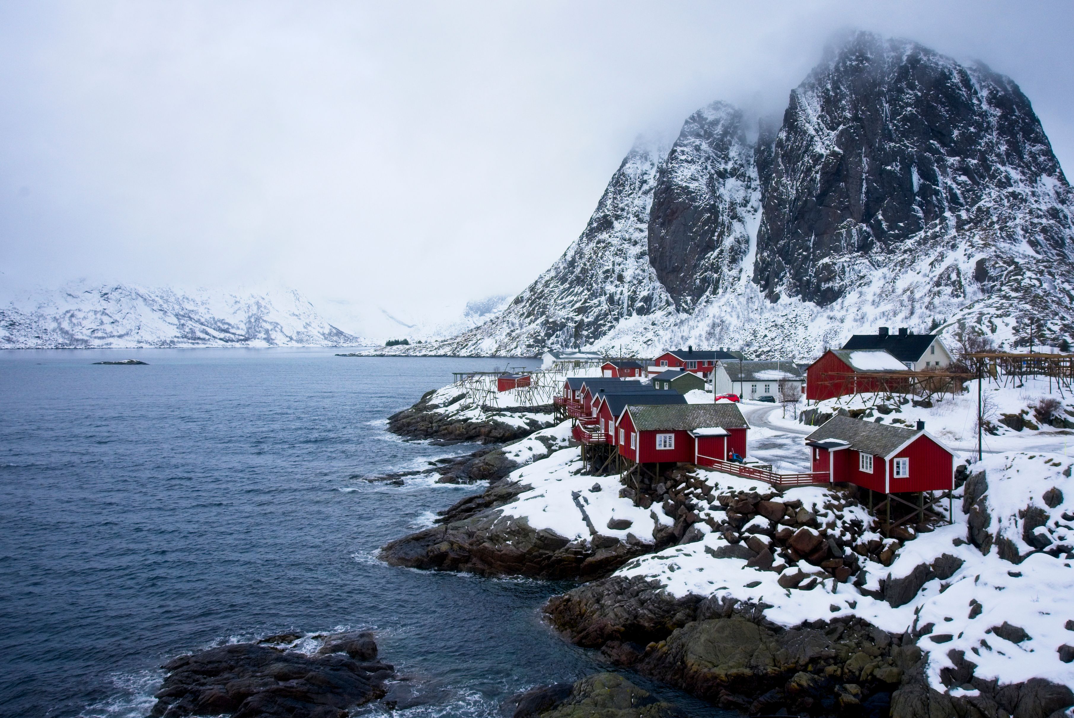 Picturesque winter scene of red cottages in Hamnøy, Norway, surrounded by snow-covered mountains and sea. - Lofoten