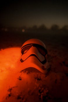 Cinematic shot of a stormtrooper helmet in snow, lit by red light at dusk.