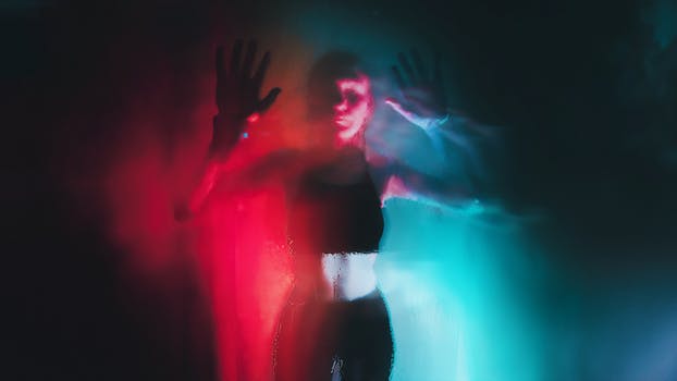 Artistic portrayal of a silhouette behind a steamy glass with colorful lighting.